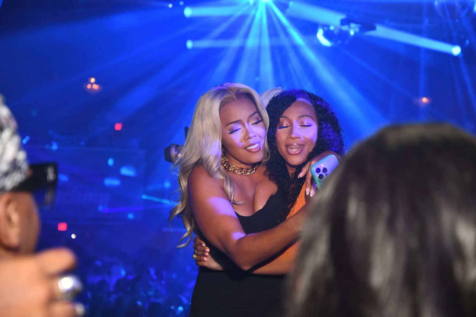 Angela Simmons singing with a friend, arms around each other, inside The Beacham